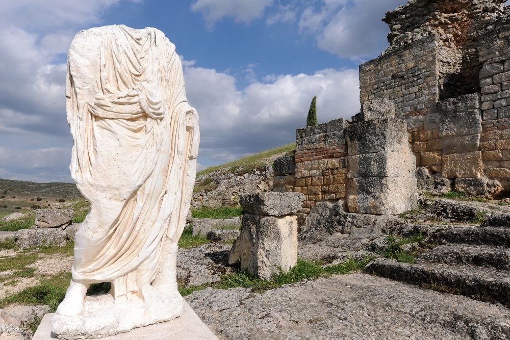 Headless statue wearing a toga in Roman ruins of Segobriga, Spain with blue skies and whispy white clouds in the background in piece about headless CMS versus monolithic CMS.