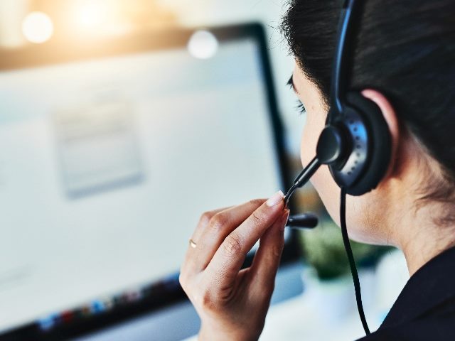 Review shot of a woman with dark hair and waring a headset and looking at a computer screen, suggesting the impact of AI in customer service. 