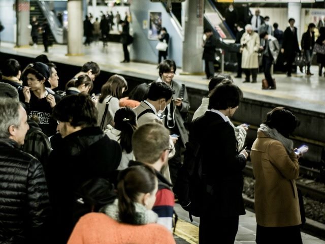 People on a train platform, many using smart devices