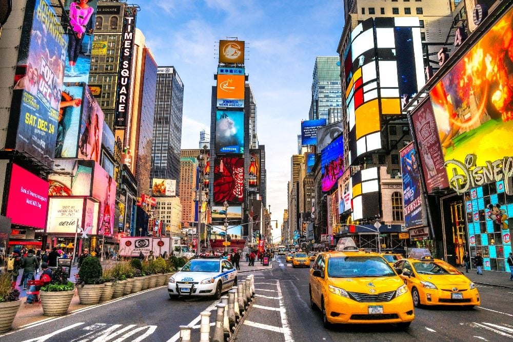 A vibrant scene of Times Square in New York City, bustling with people and traffic. The image is dominated by colorful, illuminated billboards and advertisements on tall buildings. Yellow taxis are prominent in the foreground, and the famous neon lights add to the lively atmosphere of this iconic location in piece about B2B marketing creativity.