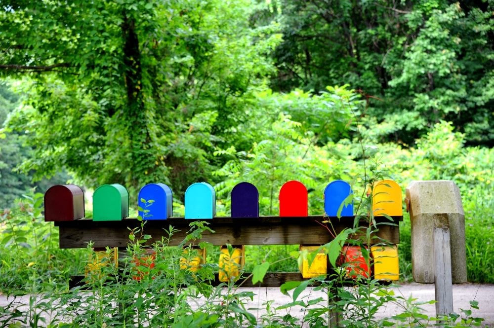 A row of mailboxes in rainbow colors sit atop a support with a sidewalk and green trees in the background in piece about email marketing trends.