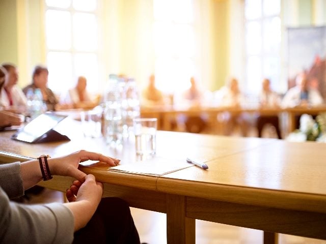 People at a round table, with one man (just his hands displayed) in the foreground. 