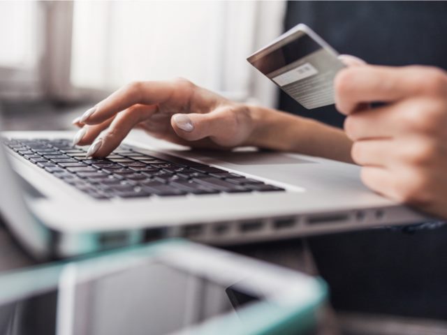 computer user holding credit card and entering data via his keyboard.