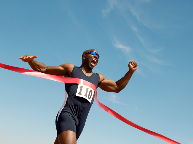 A male runner winning race against blue sky breaking the tape