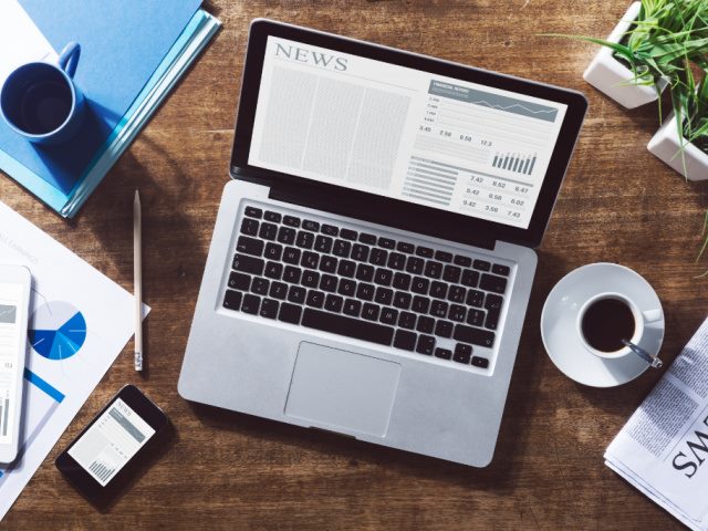 computer on a desk with news showing on screen
