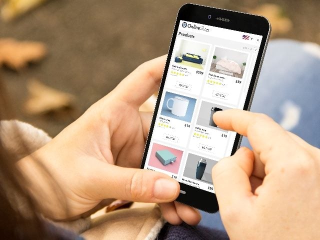 A person holds a phone while sitting in a park and shopping on an e-shop site on a smartphone in piece about mobile first ecommerce. 