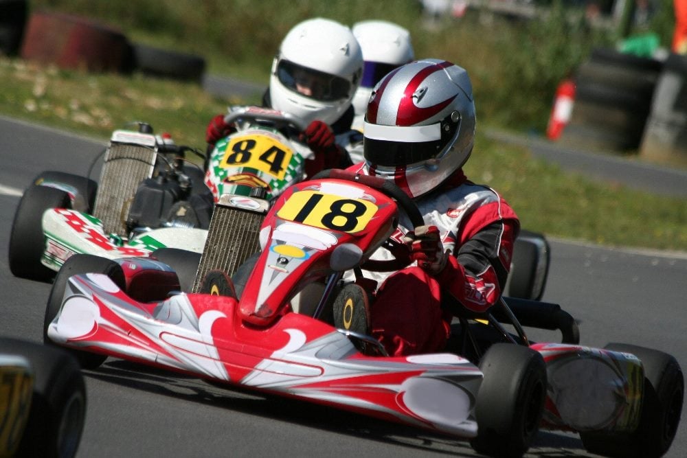A close up of a go-kart race with young drivers wearing helmets in red and white and in red, white and green go karts with yellow and black participant number signs with 84 and 18 visible in piece about emotional marketing.