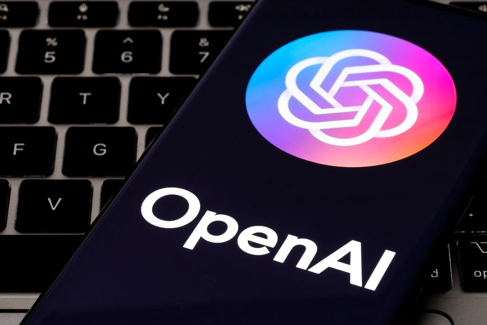 The OpenAI name and logo are visible on a smartphone that is perched on top of a computer keyboard in piece about OpenAI's customizable GPTs.