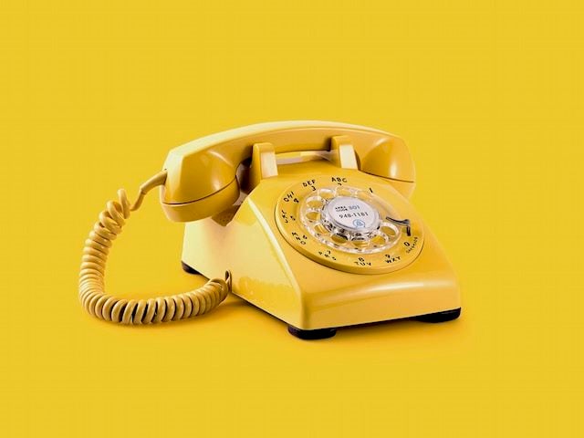 isolated yellow rotary phone against a matching yellow background