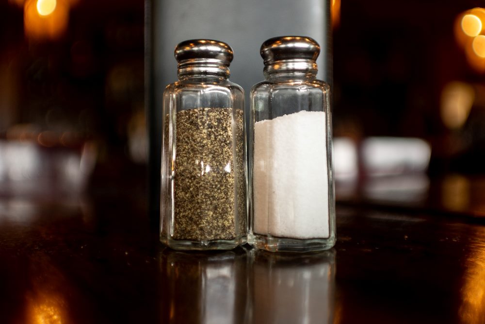 Salt and pepper shakers sit on a table in front of a black menu in a restaurant in piece about sales and marketing alignment.