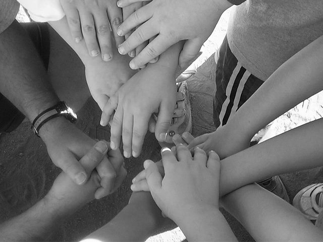 A black and white photograph of children's hands together in a huddle. 