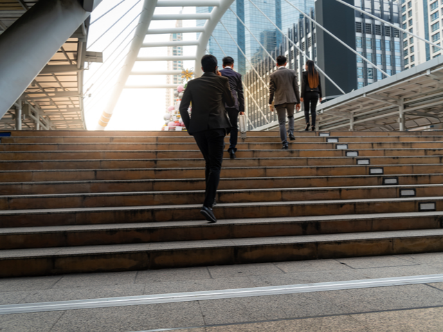 Businessmen and woman walking up the stairs in the downtown area that is full of tall buildings. Return to work concept