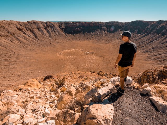 A man in the desert looking out over a giant meteors impact crater