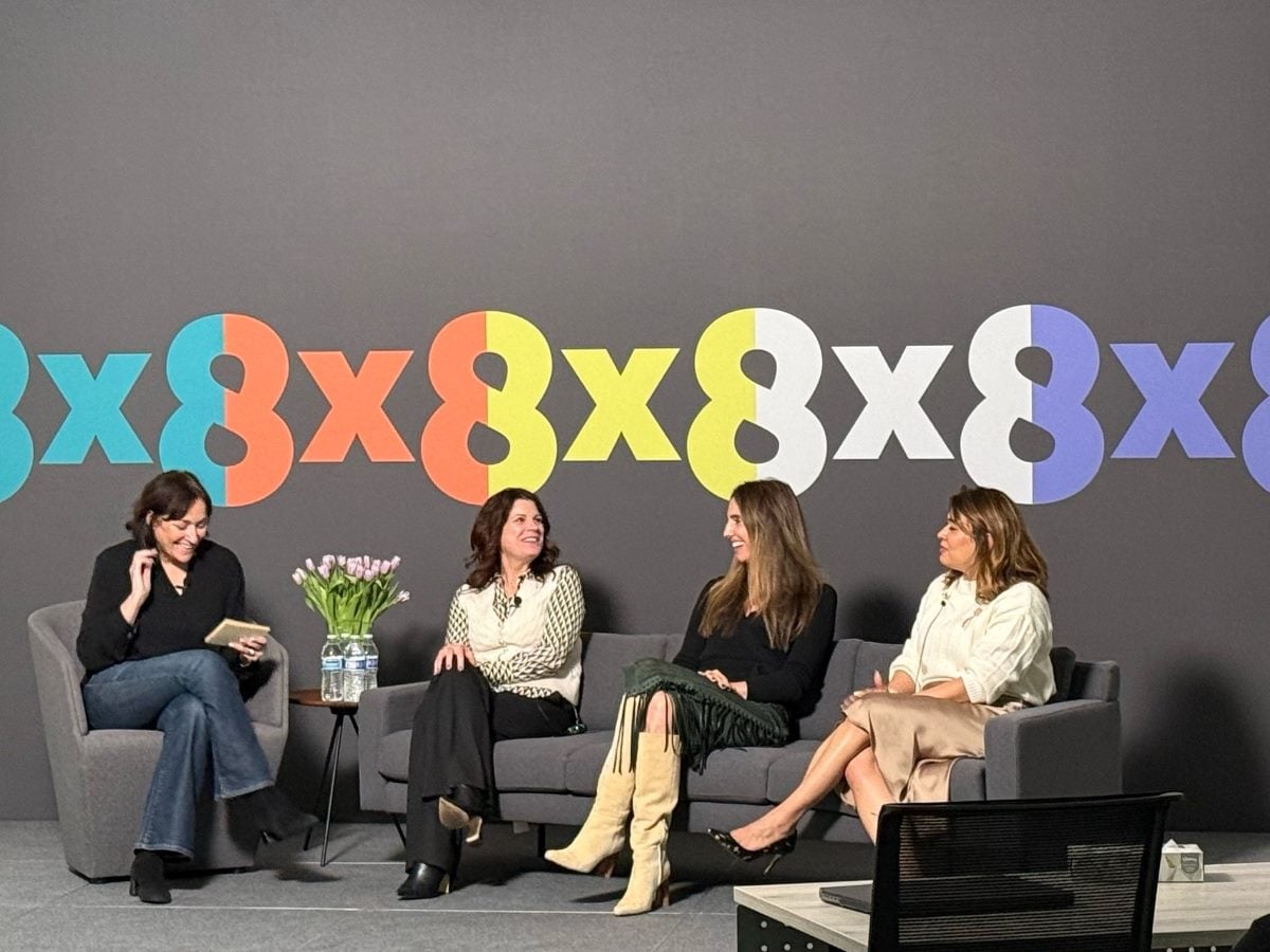 Four women on a stage in a panel sitting, with 8x8 logos on the back wall.