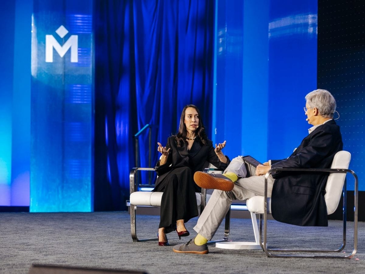 Paloma Paraja, customer experience manager at Santalucía Seguros, speaks on stage with Medallia CEO Sid Banerjee during a live session at Medallia Experience ’26, seated in white chairs against a blue conference backdrop featuring the Medallia logo.