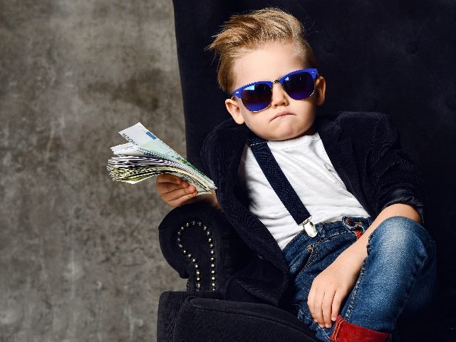 Young boy sits holding a bundle of money in big luxury armchair, symbolizing the need for marketers to unlock marketing budgets. 