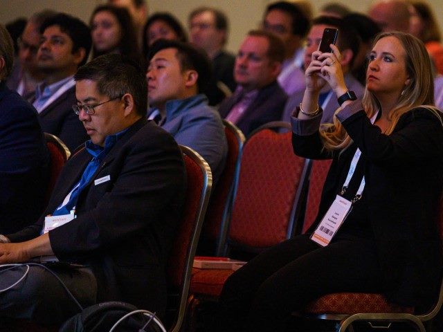A woman taking a picture sitting down among a crowd at the MarTech Conference in Boston.