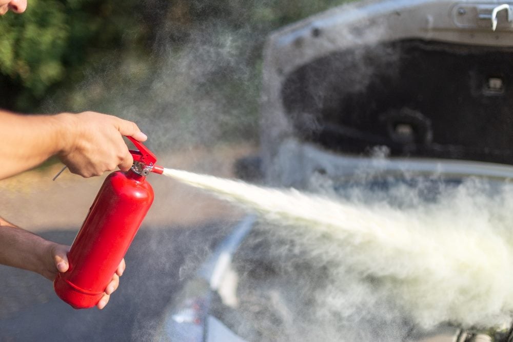 A person is holding and using a red fire extinguisher on a smoking engine of a car with an open hood in piece about the voice of the customer with AI.