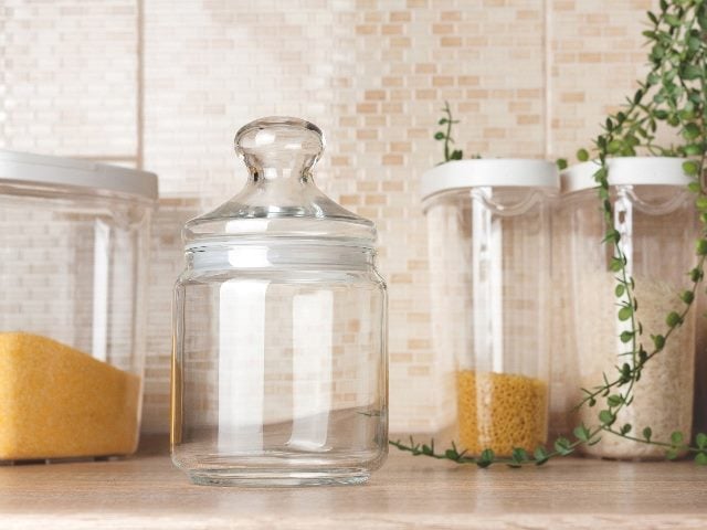 Four glass jars on counter, one empty and the other three with baking powders.