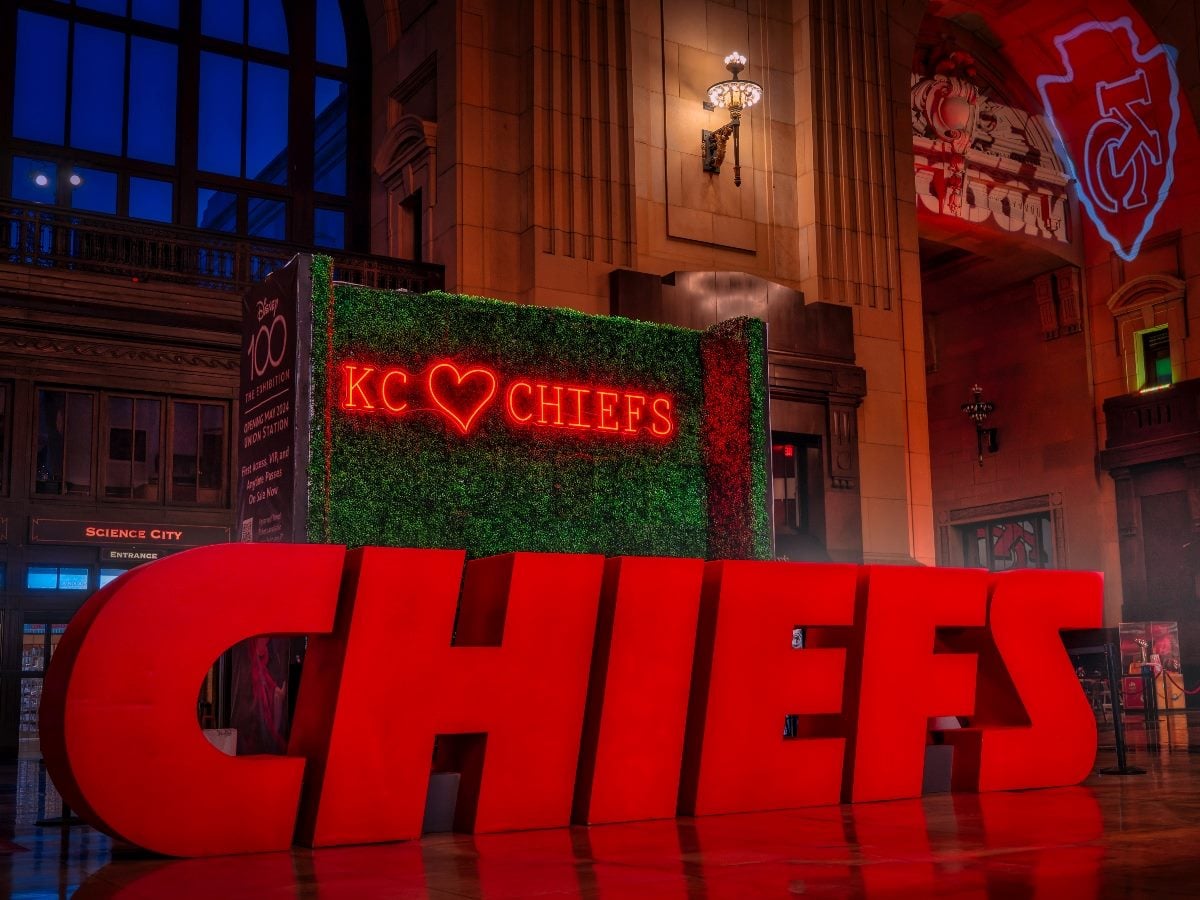 Large red “CHIEFS” letters displayed inside Kansas City’s Union Station, with a glowing “KC ♥ Chiefs” sign illuminated in red behind them at night.
