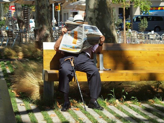 Man sitting on a bench outside reading a newspaper.