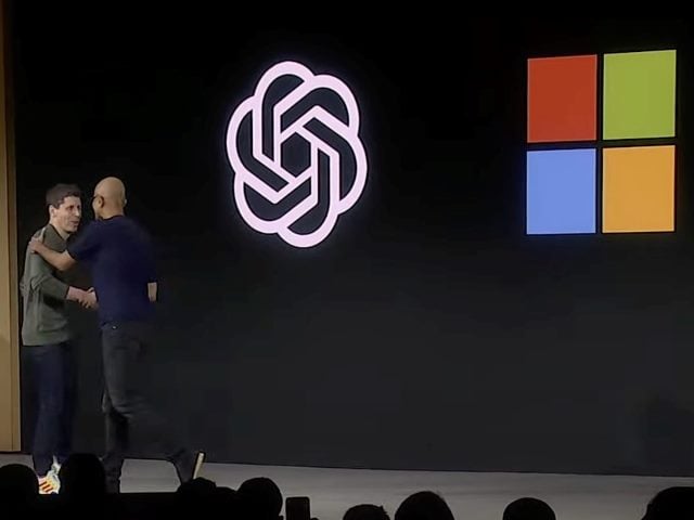 A screenshot from a YouTube video of Microsoft CEO Satya Nadella embracing former OpenAI CEO Sam Altman on stage at OpenAI's developer conference in November 2023.
