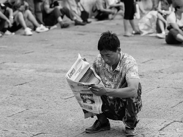 Man scooting down reading a Chinese newspaper.