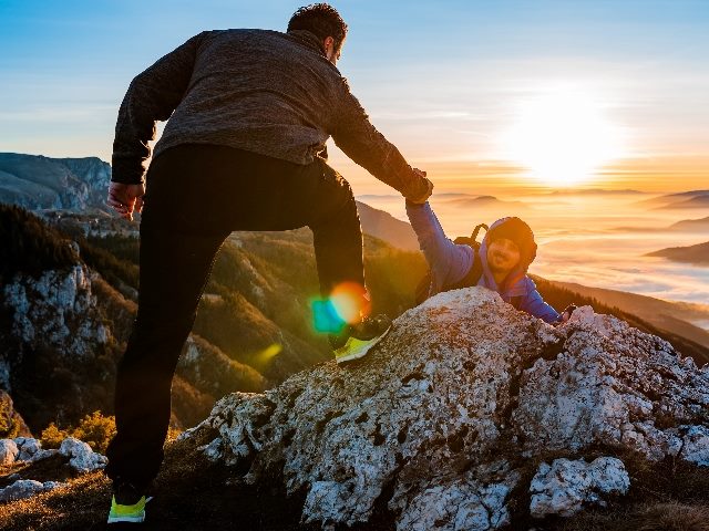 Man reaching out hand to a fellow male mountain-climber to help get to the top.
