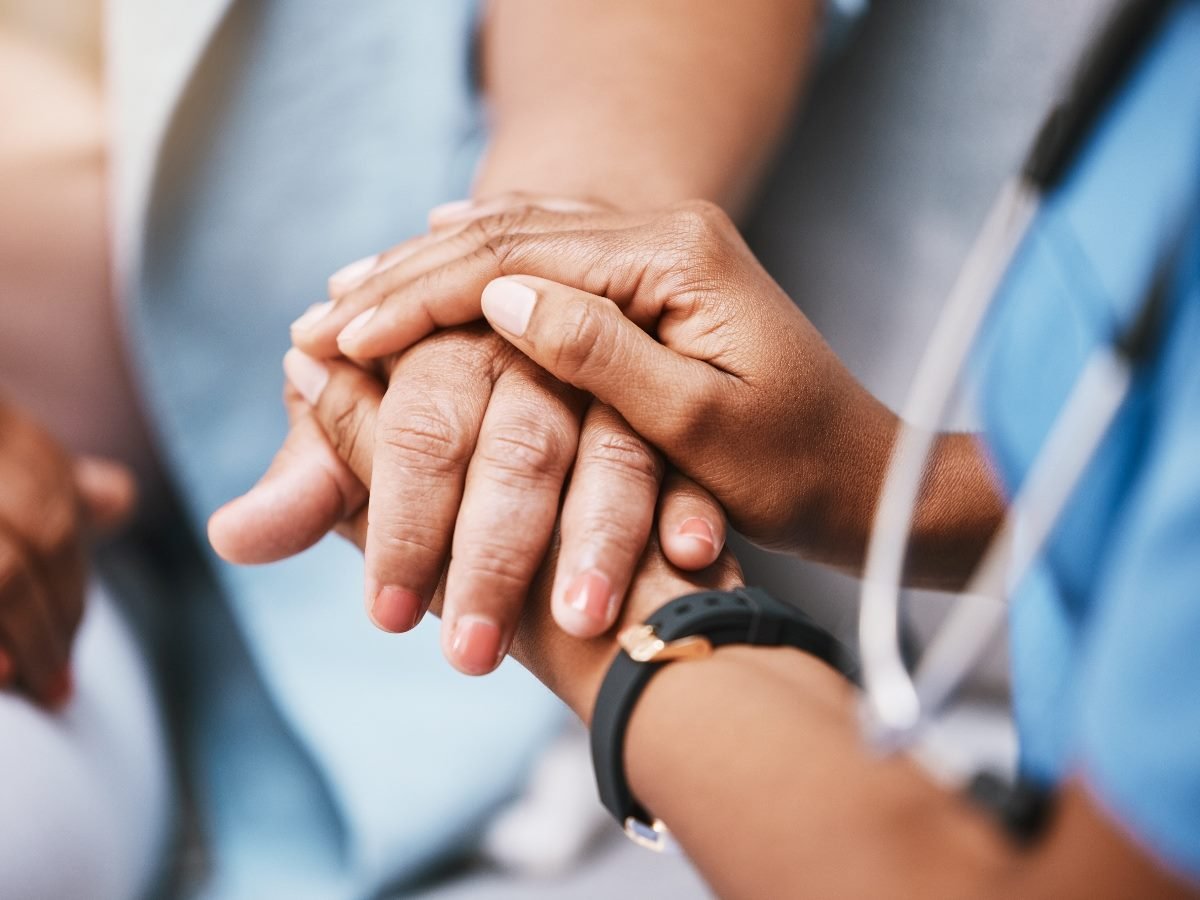 A healthcare professional gently holding a patient’s hand in a comforting gesture, symbolizing compassion and trust in medical care.