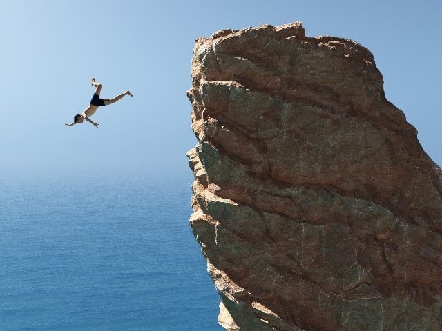 Man jumps into the ocean off large rock. 