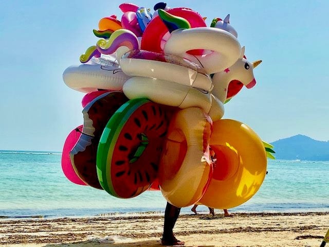vendor standing on sunny beach with a number of flotation devices for sale