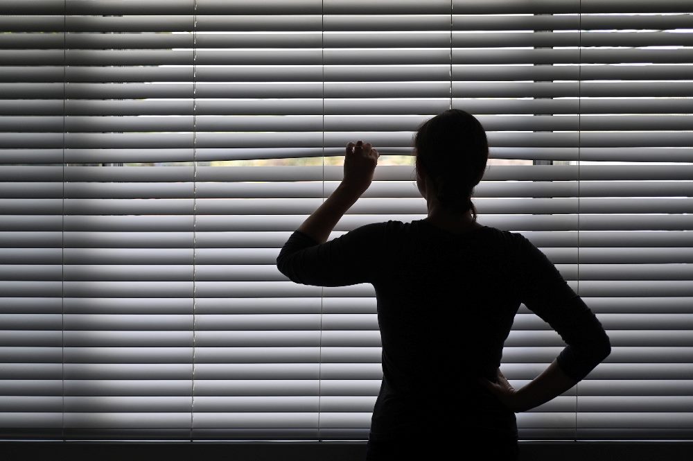 A person with their back turned looks out through white venetian blinds in piece about data privacy.