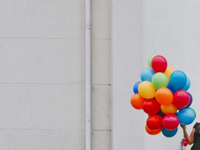 woman's arm holding a large group of brightly colored balloons