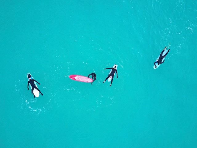 four surfers resting on their boards in very very blue water