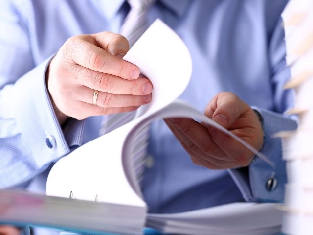 A person wearing business attire and sitting at a desk goes through pages of compiled documents in piece about user onboarding. 