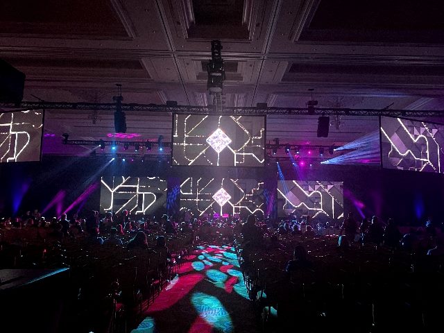 A brightly lit hall with aqua, magenta and white lighting and an audience in attendance at the Medallia 'Experience '24 conference in Las Vegas. 