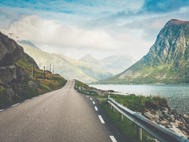 Empty road with mountains and lake as backdrop.