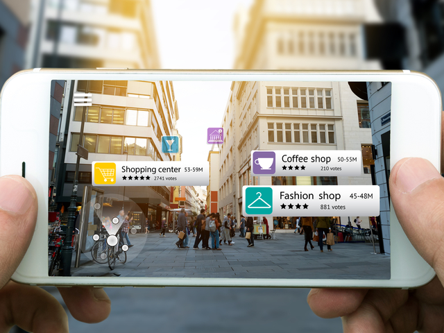 A hand holding a smartphone using an AR application to check out relevant information about the spaces around the customer. City background