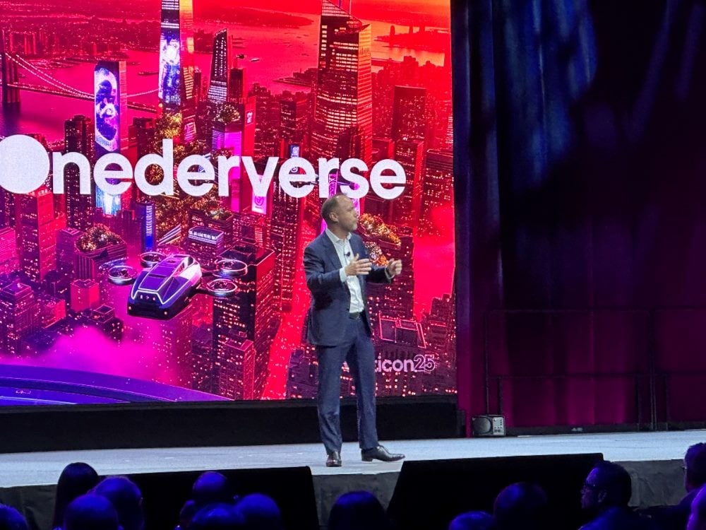 Optimizely CEO Alex Atzberger speaking on stage at Opticon25 in New York City, with a vibrant “Onederverse” backdrop behind him.
