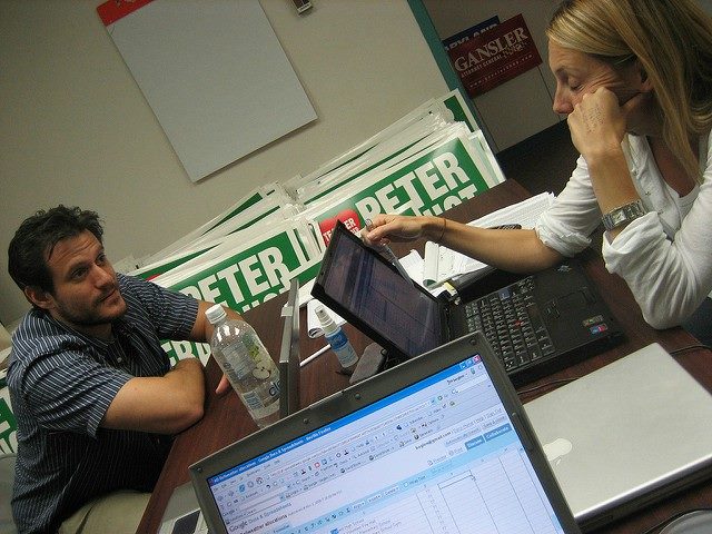 A man and a woman sitting at a table with laptops on it.