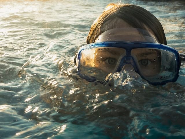underwater swimmer peeking up with goggles on