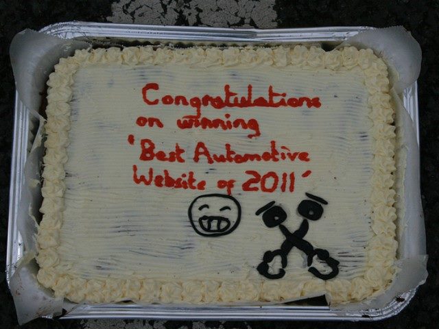 Cake with white frosting and red words written on it that say, "Congratulations on winning 'Best Automotive Website of 2011'"