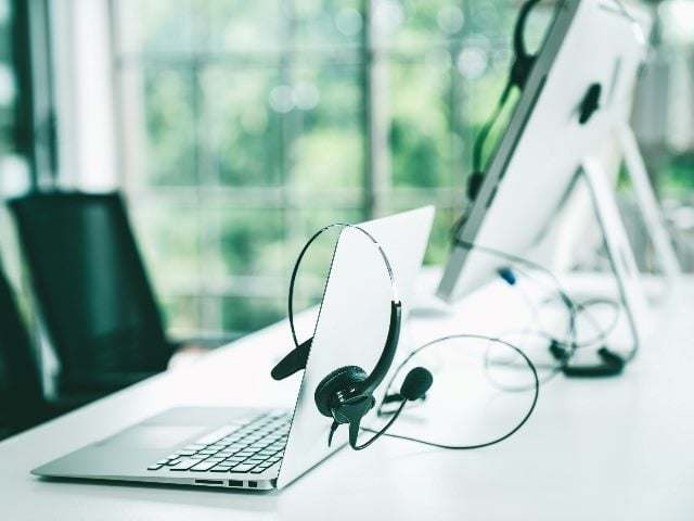Headset and customer support equipment (including a laptop and desktop computer) on a desk with two chairs at call center ready for actively service.
