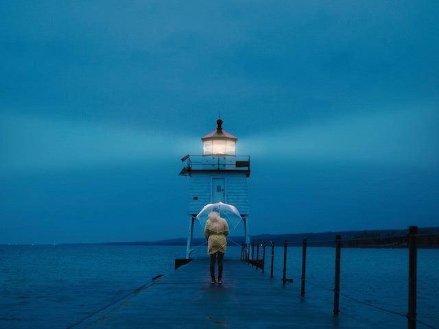 person standing in front of a lighthouse at night, with clear umbrella overhead