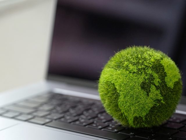 An open laptop with keyboard and screen visible and with a green globe of the world sitting on the keys in piece about sustainable website design.