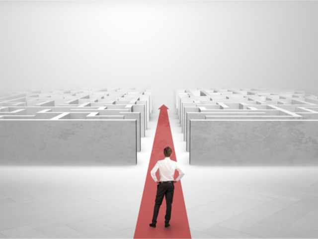 A businessman cutting a path and rolling a red carpet through the heart of the maze - Reducing IT complexity concept