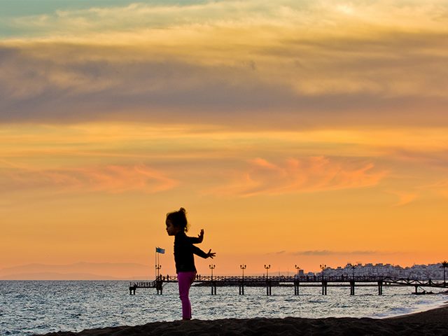 Young girl standing on the beach at sunset with her arms stretched out in elation. 