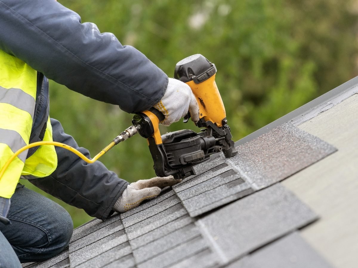 Worker using pneumatic nail gun install tile on roof of new house under construction.