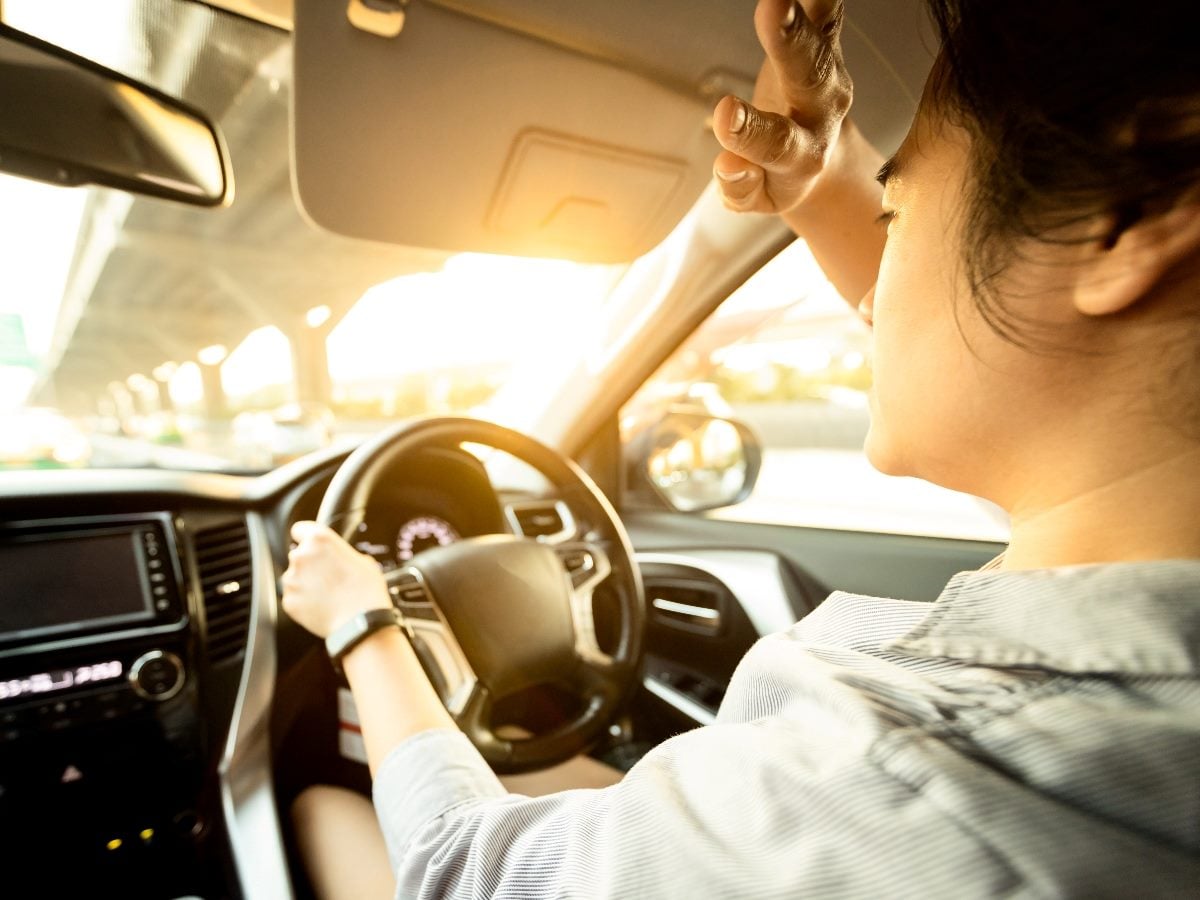 Woman driving and blocking a strong sun by putting her hand to her forehead.