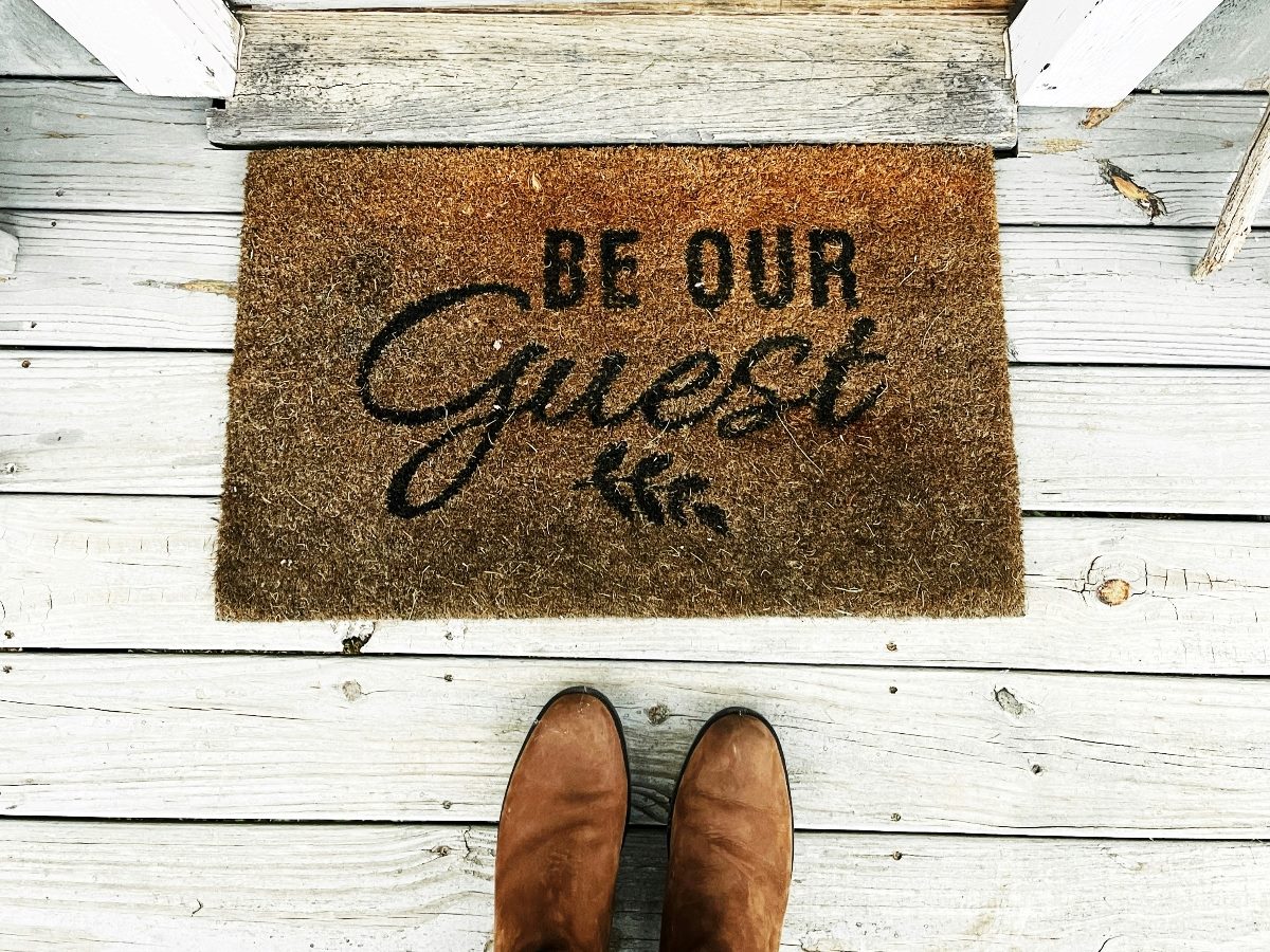 Shoes in front of a welcome mat that says, "Be Our Guest."